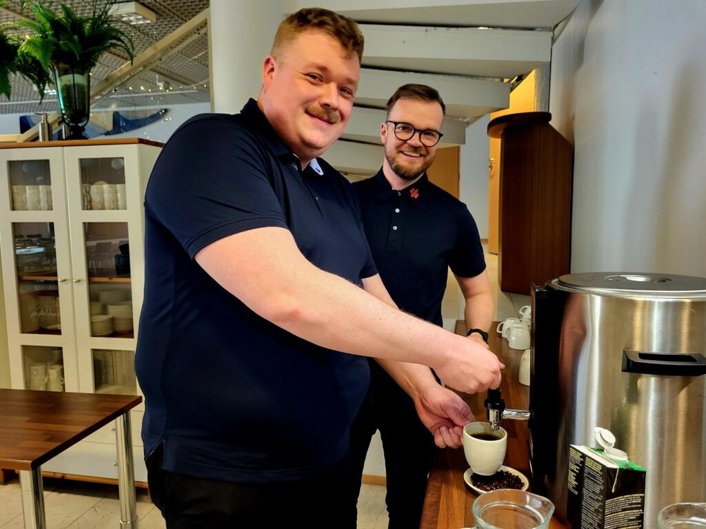 Miikka Oksanen ja Miro Ulvinen seisovat ja ovat ottamassa kahvia kahviautomaatista.