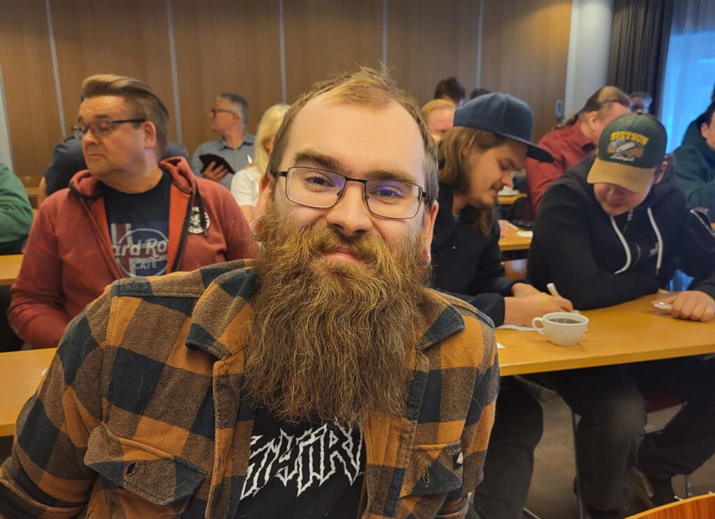 Nuori parrakas mies ruutupaita päällään on kokouspaikalla.