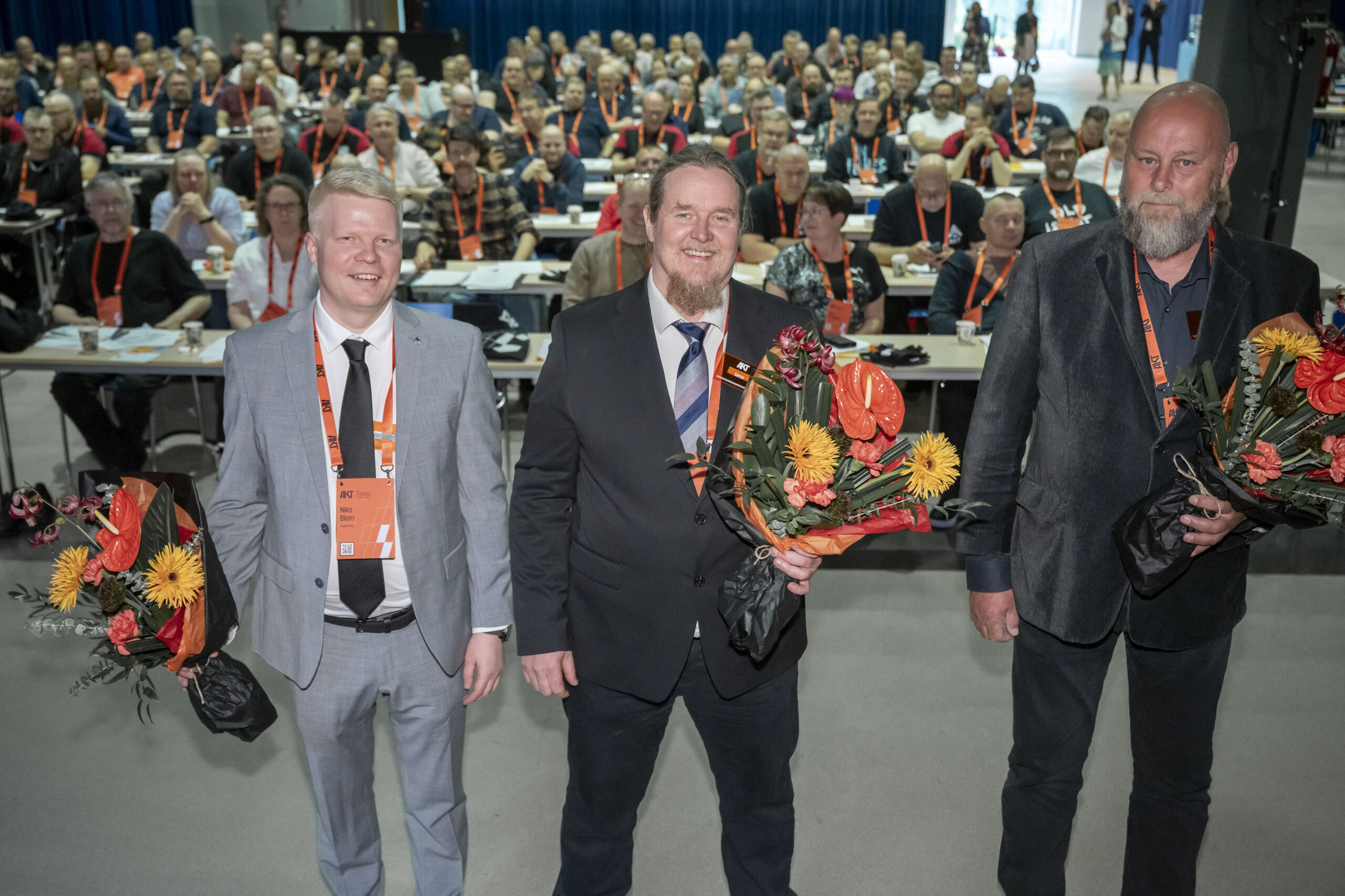 Kuvassa vasemmalla vaaleassa puvussa kravatti kaulassa Niko Blom kukkakimppu kädessään, keskellä tummassa puvussa Ismo Kokko myös kukkakimppu kädessään, oikealla Juha Anttila. Miehet on valittu AKT:n puheenjohtajaksi ja varapuheenjohtajiksi.