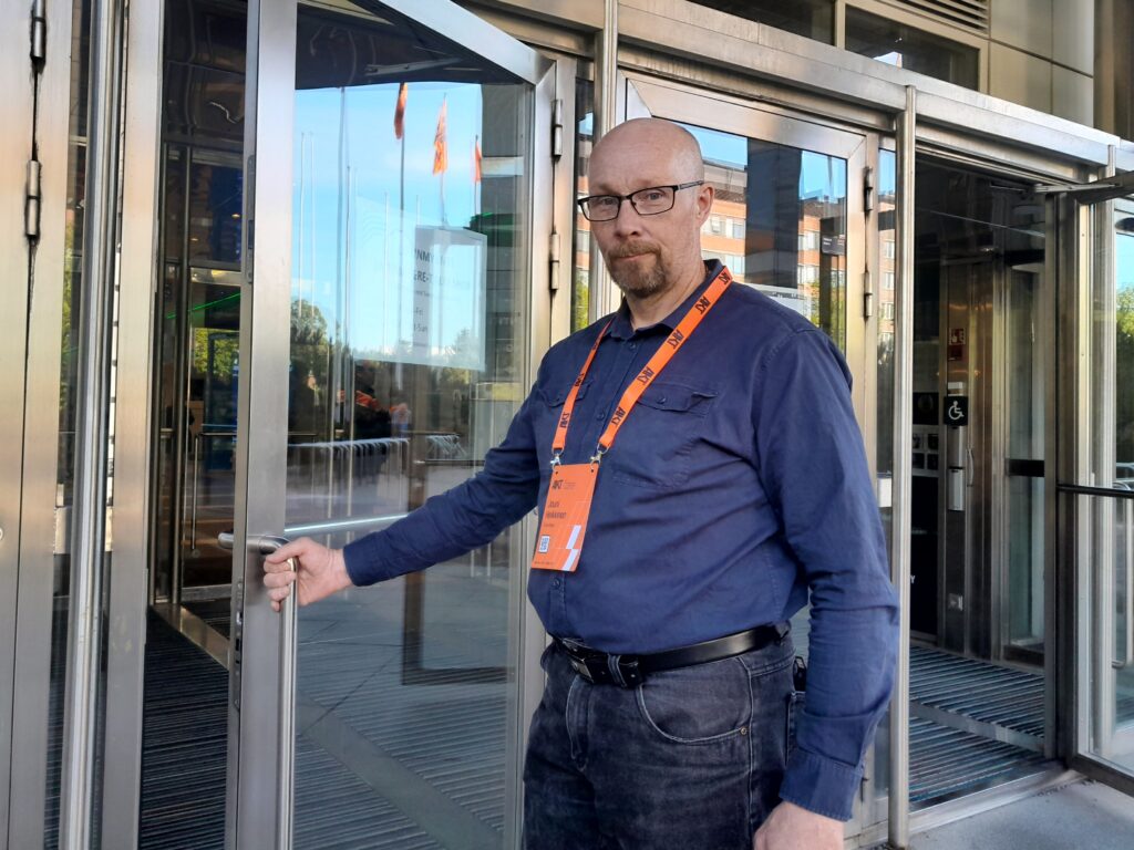 Mies sininen paita päällään Tampere talon ovella käsi kiinni ovenkahvassa