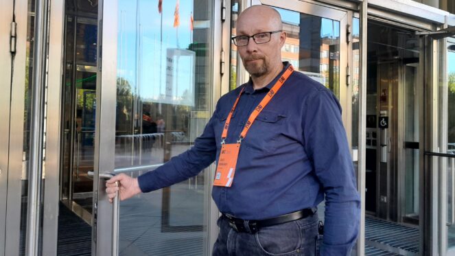 Mies sininen paita päällään Tampere talon ovella käsi kiinni ovenkahvassa