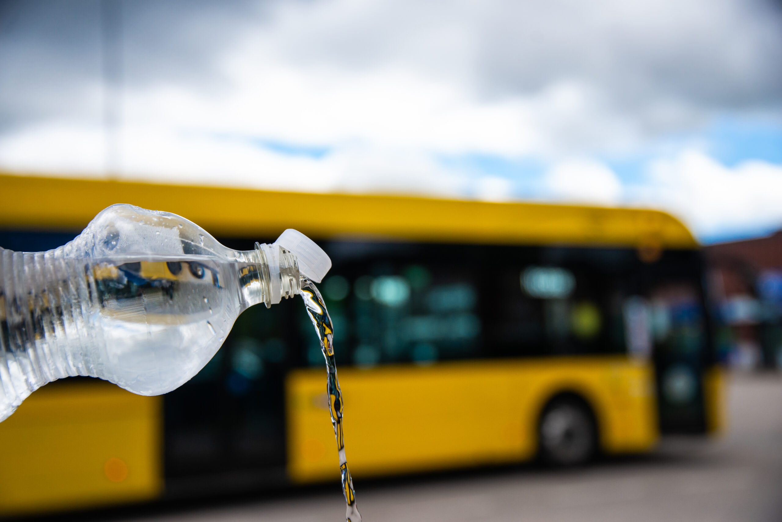 Kuva keltaisesta bussista, jonka edustalla on vesipullo josta kaadetaan vettä.
