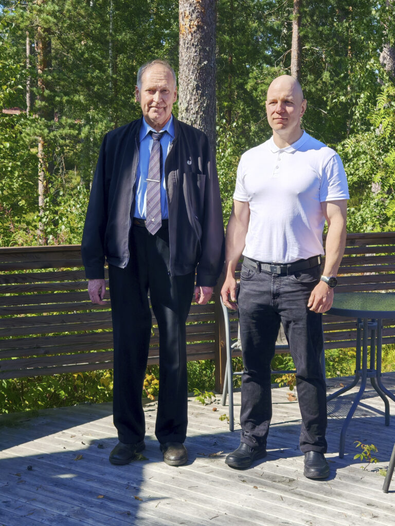 Kuvassa kaksi henkilöä seisoo terassilla kesäisessä valossa.