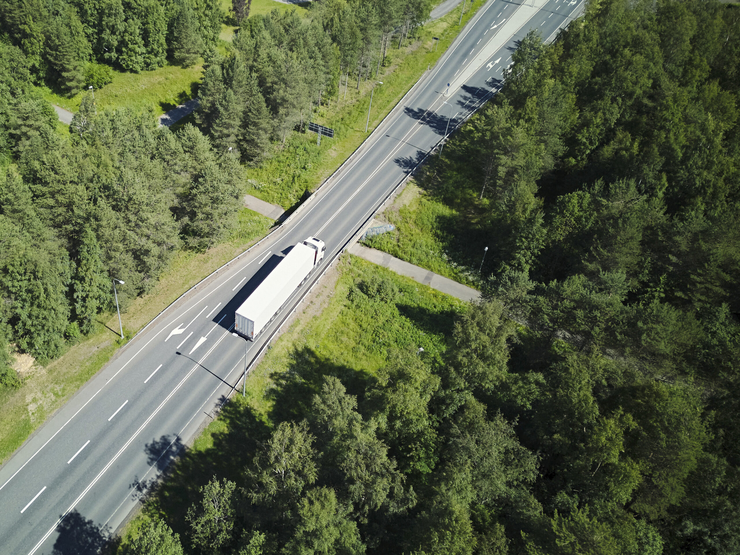 Kuva vehreästä maisemasta ja valkoisesta kuorma-autosta ajamassa tiellä lintuperspektiivistä otettuna.