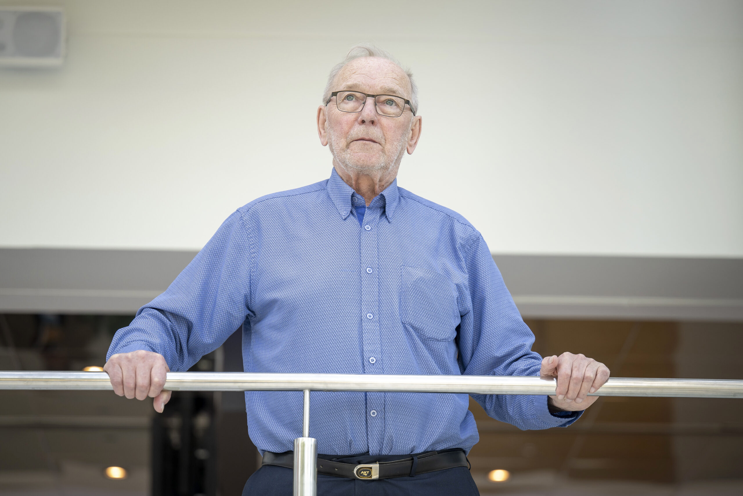 Kuva sinisessä kauluspaidassa olevasta Kauko Lehikoisesta seisomassa vasten kaidetta ja katsomassa yläviistoon.