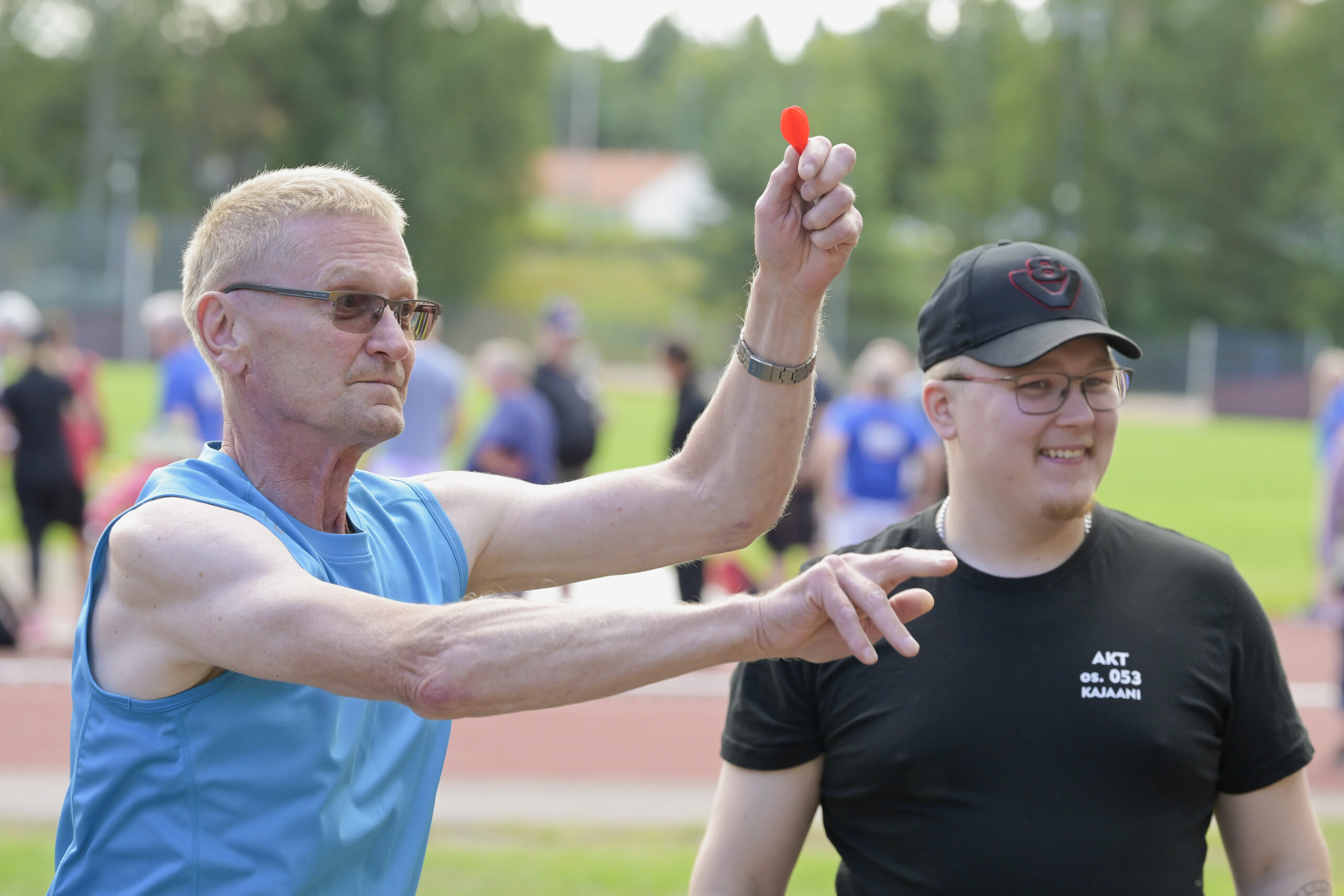Sinipaitainen henkilö heittää tikkaa, taustalla mustapaitainen henkilö.