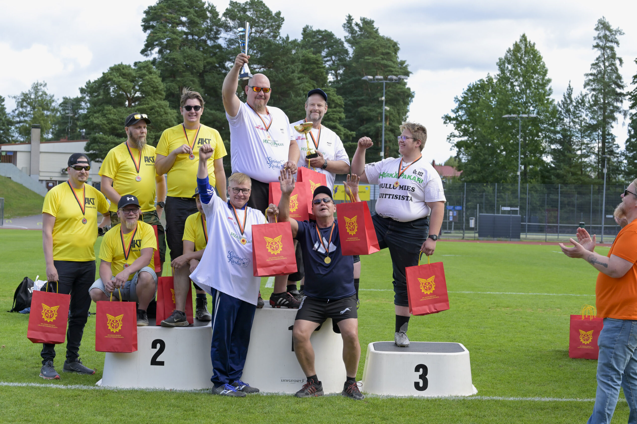Joukkueet poseeraavat palkintopallilla nurmikentällä.