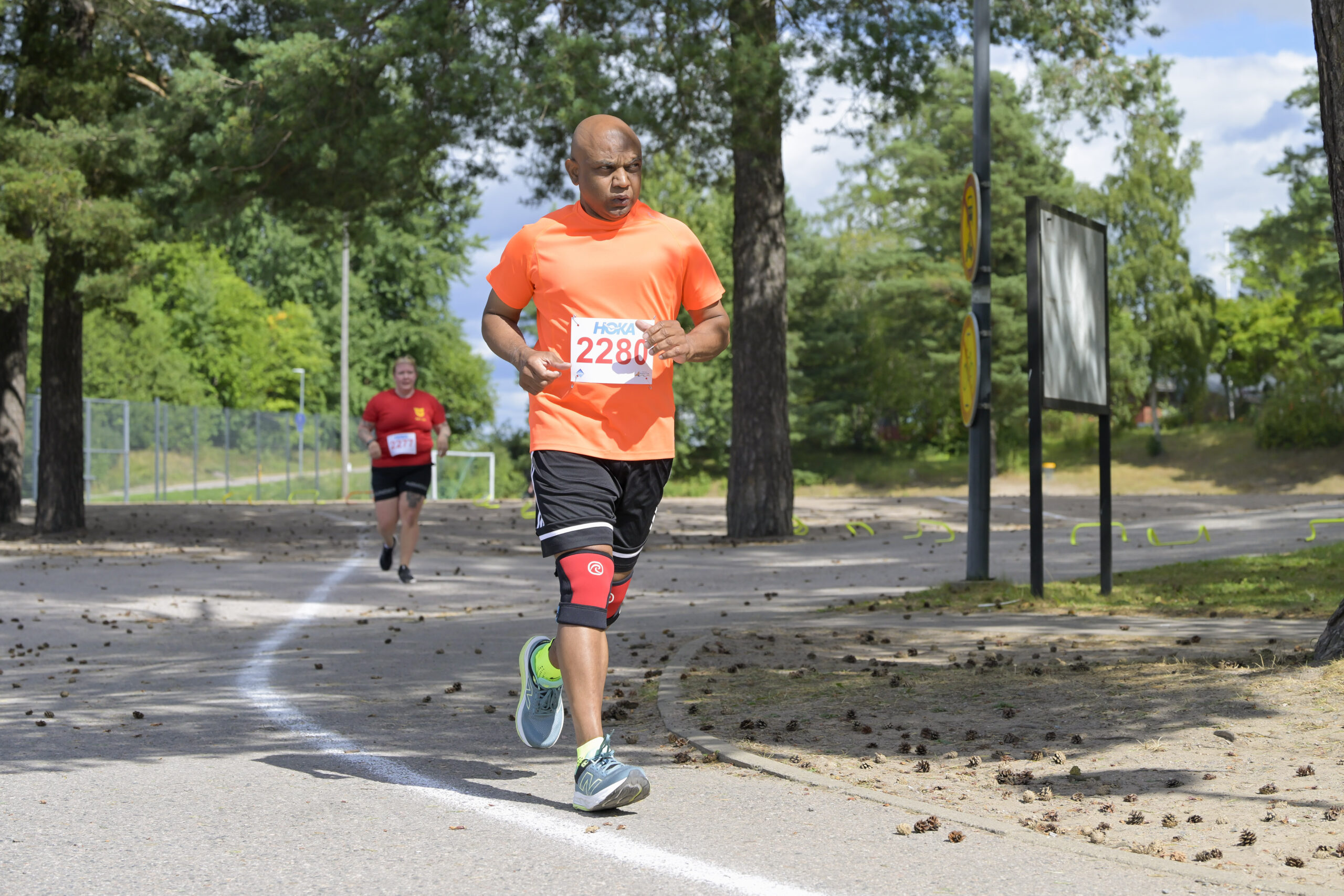 Oranssissa paidassa oleva henkilö juoksee puiden ympäröimänä.