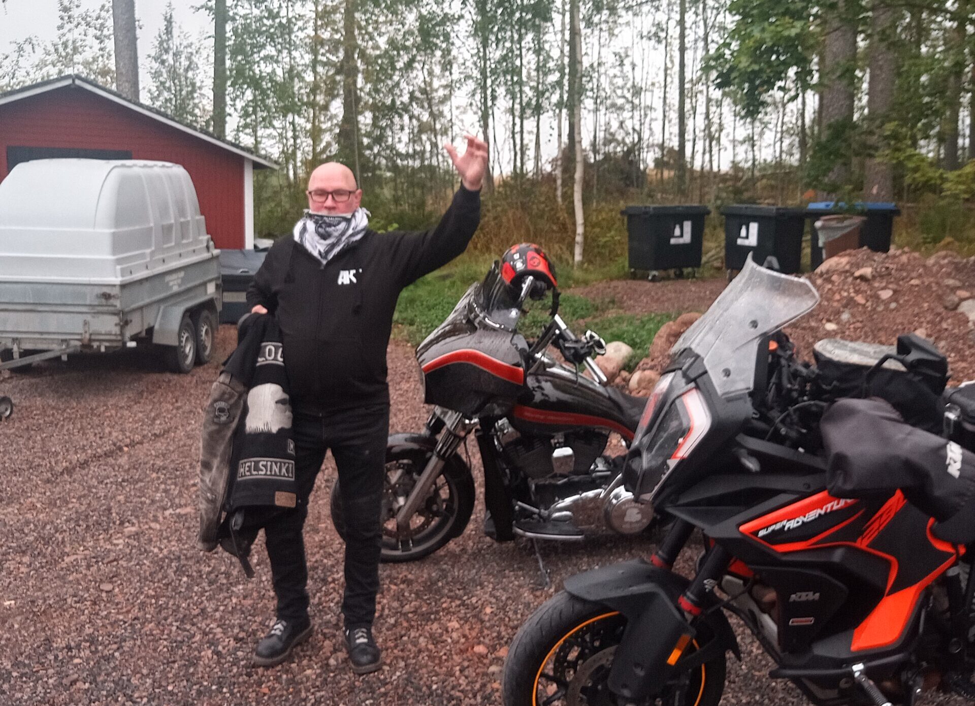 Kaljupäinen henkilö vilkuttaa moottoriajoneuvojen edustalla.