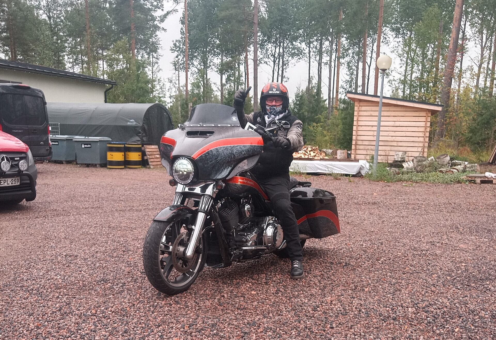 Kuvassa henkilö näyttää peukkua paikallaan olevasta moottoripyörästä.