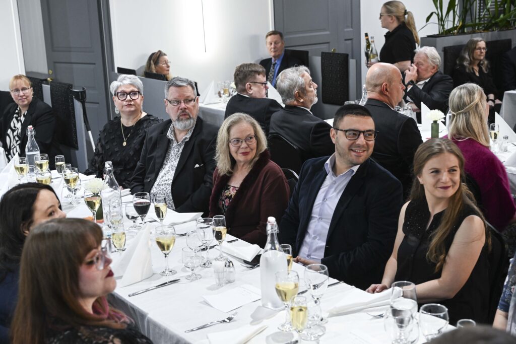 Juhlaväkeä valkoisella pöytäliinalla ja juhlavilla astioilla katetun pitkän pöydän äärellä.
