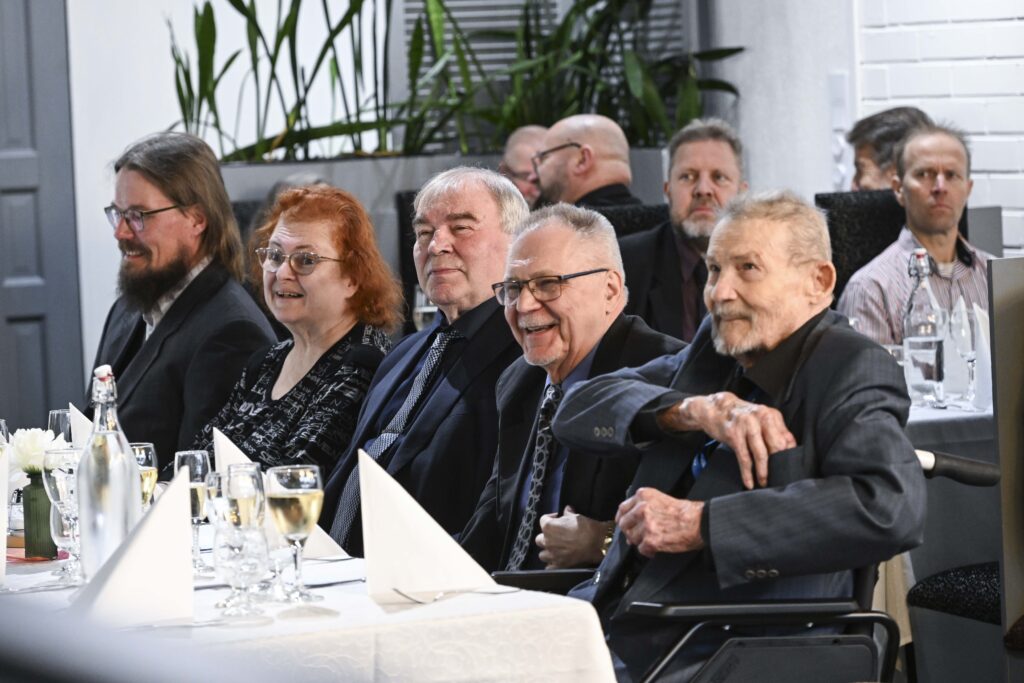 Iloista hieman iäkkäämpää juhlaväkeä katetun pöydän äärellä kuohuvat edessään.