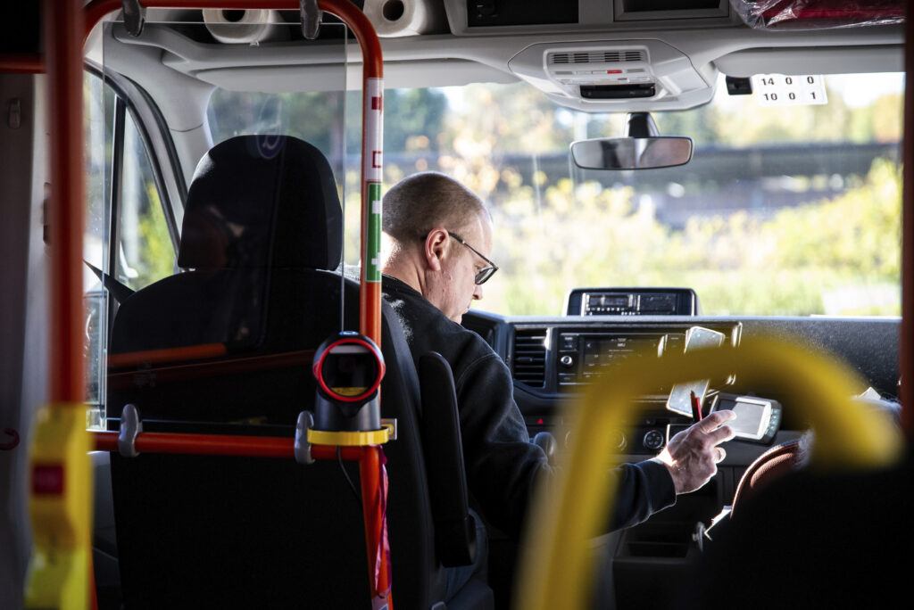 Mies istuu pikkubussin kuskin paikalla kynä kädessään.