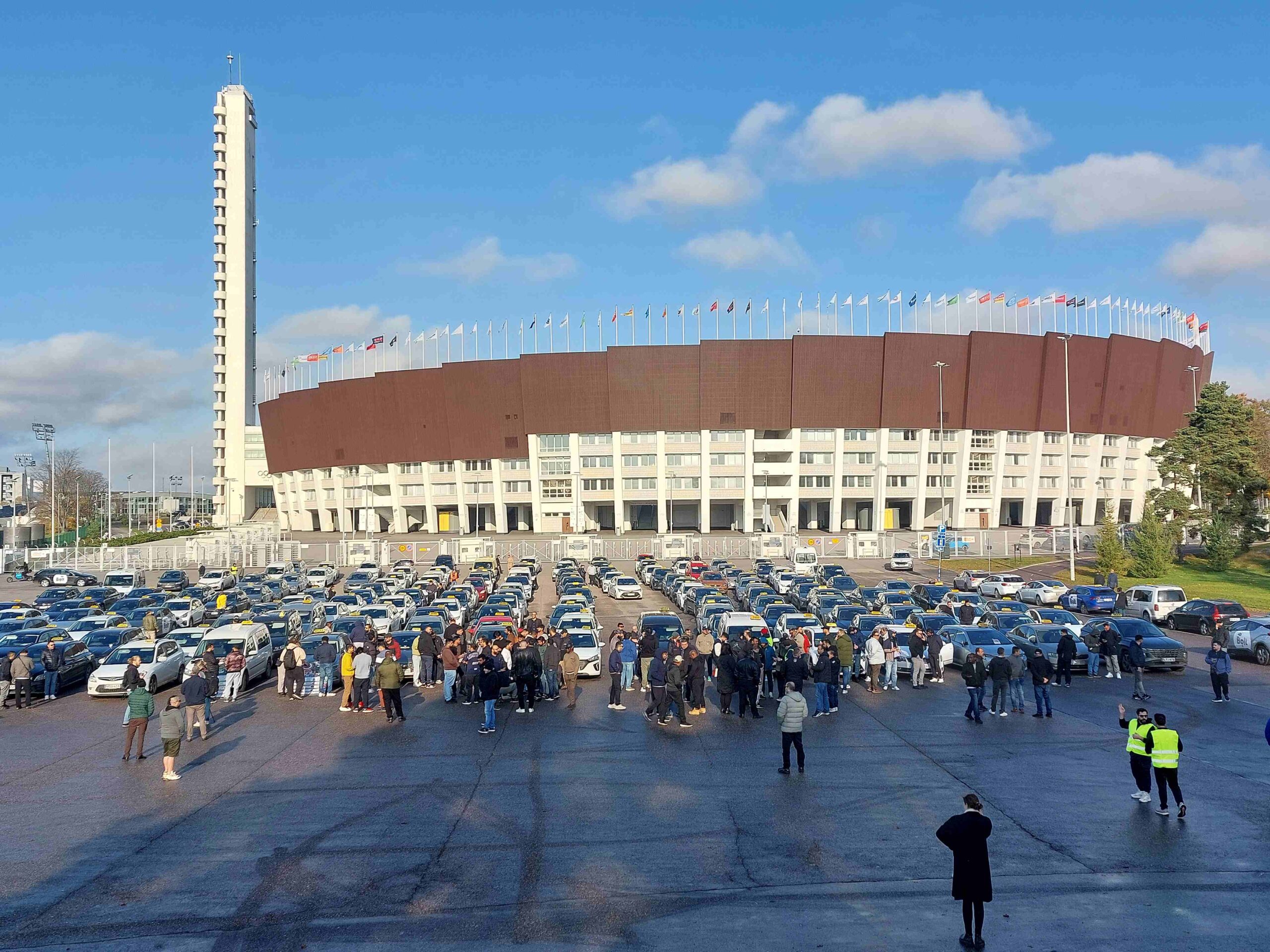 Olympiastadionin parkkipaikalla kymmeniä Bolt ja Uber-takseja, joiden kuljettajat ovat osoittamassa mieltään.