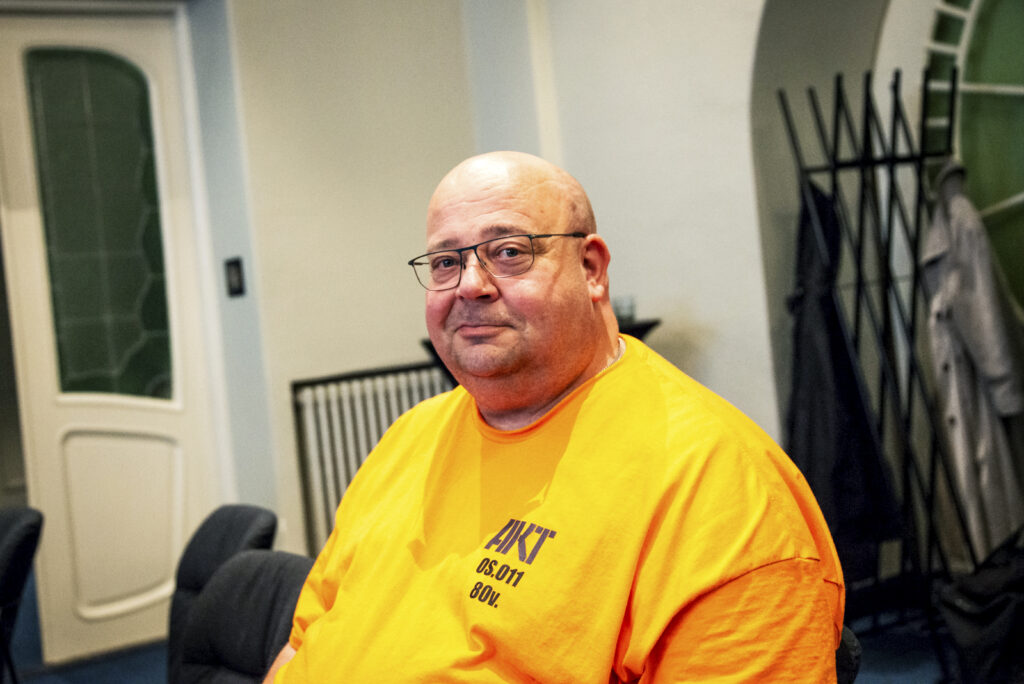 Mies hymyilee vienosti oranssikeltaisessa paidassa.