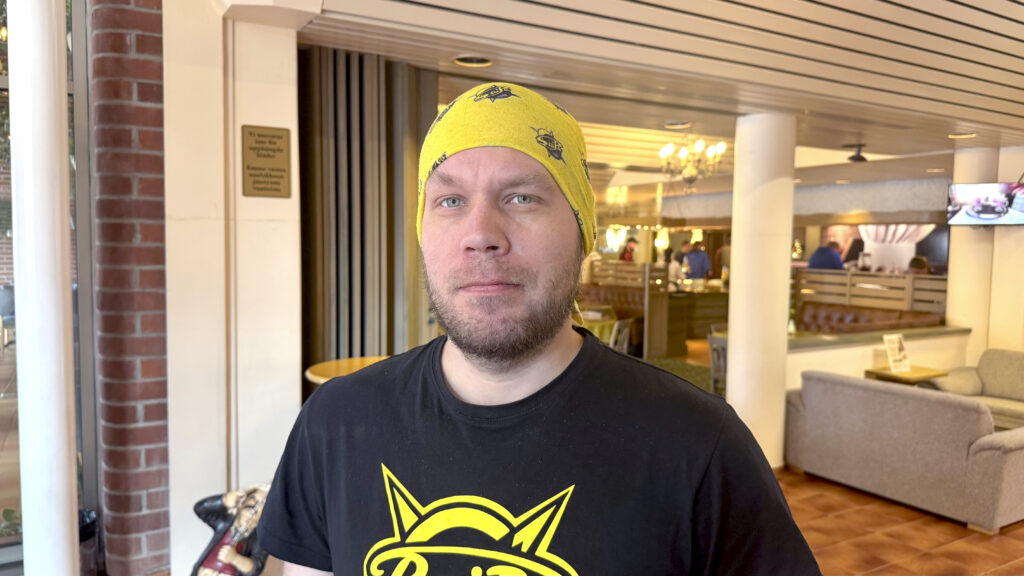 Mies keltaisessa päähineessään ja mustassa paidassa, jossa on keltainen elementti.